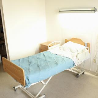 A hospital patient room featuring a bed with a blue blanket.