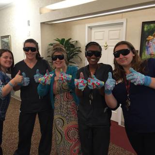A group of people indoors, wearing sunglasses and smiling, giving thumbs up.