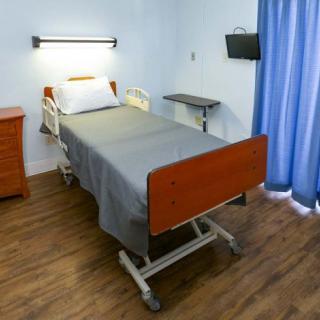 A hospital room featuring a single bed with gray linens, a bedside table, and a TV.