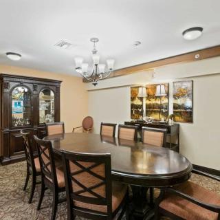 A spacious dining room with a large table, surrounded by chairs, featuring a chandelier and wooden cabinet.