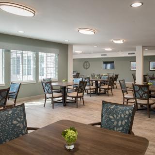 A modern dining area with multiple tables and chairs, featuring ample natural light.