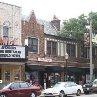 Street view of a theater marquee and adjacent shops with parked cars.