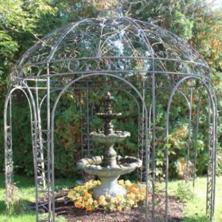 A decorative fountain within a metal gazebo in a garden setting.