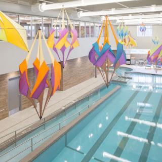 An indoor swimming pool featuring colorful geometric art installations hanging from the ceiling.