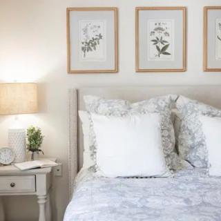 A cozy bedroom featuring a bed with patterned bedding, white pillows, and framed botanical artwork above the headboard.