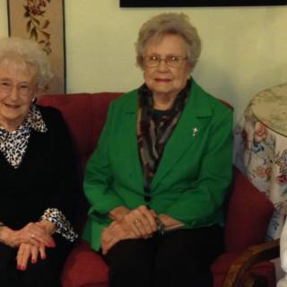 Two elderly women sitting on a couch in a living room.