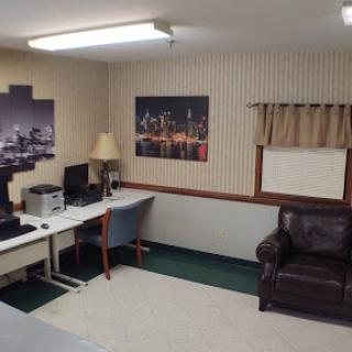 A cozy office space featuring a work desk, computer setup, comfortable chair, and a sofa, complemented by cityscape wall art.
