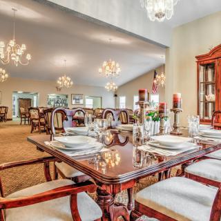 An elegant dining room with ornate chandeliers, a polished wooden table set for a meal, and classic furniture.