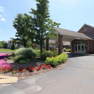 A well-landscaped building entrance with colorful flower beds and a tree on a sunny day.