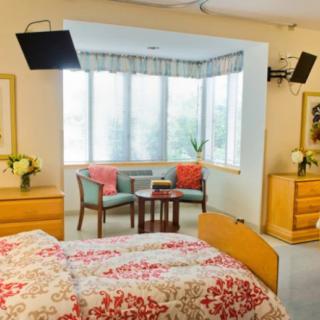 A well-lit hospital room with floral bedding and comfortable seating by a large window.