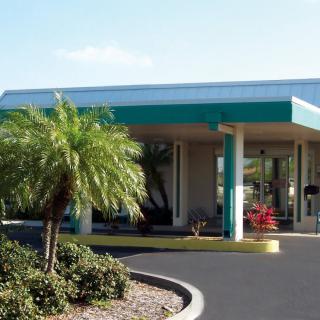 A building entrance with a palm tree and landscaped driveway on a sunny day.
