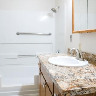 A modern bathroom featuring a granite countertop sink and a spacious shower area.
