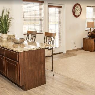 A cozy kitchen interior featuring a wooden counter with chairs, large windows, and stylish decor.