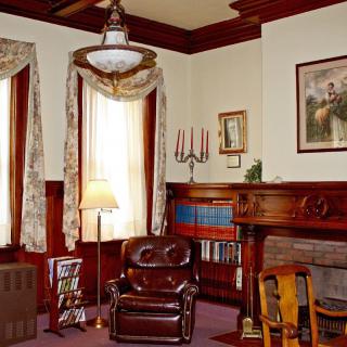 A vintage living room featuring a leather armchair, fireplace, and bookshelves, adorned with wooden accents and classic decor.
