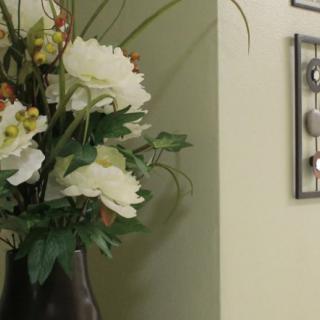 A decorative arrangement of white flowers in a vase beside a wall adorned with framed art.