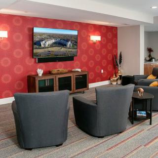 A modern living room with gray chairs, a flat-screen TV, and vibrant red patterned wallpaper.