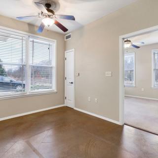 A clean, bright room with a ceiling fan, large window, and doorway leading to another space.