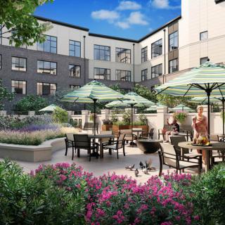 A beautifully landscaped courtyard with patio seating and umbrellas, surrounded by a multi-story building.