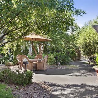 A serene garden patio with a table, chairs, and an umbrella surrounded by lush greenery.