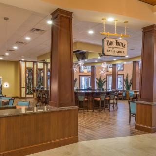 Cozy restaurant interior with a dining area and bar, featuring wooden pillars and warm lighting.