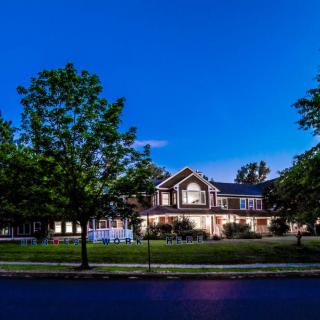 A well-lit residential house at night, surrounded by trees and a neatly manicured lawn.