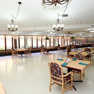 A bright and spacious dining area featuring tables and chairs, illuminated by elegant chandeliers.