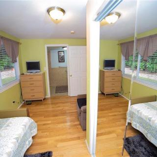 A cozy bedroom with twin beds, hardwood flooring, mirrored closet, and dressers equipped with televisions.