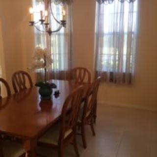 A dining room with a wooden table set, chandelier, and windows with sheer curtains.