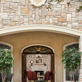 A charming stone facade with an arched entryway leading to a cozy outdoor seating area adorned with potted plants.