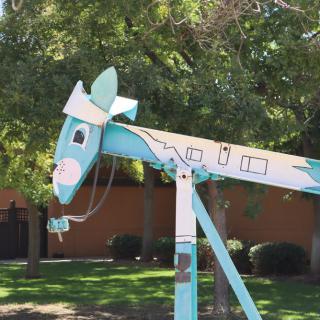 A whimsical blue metal horse sculpture standing outdoors surrounded by trees.