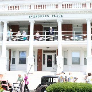 A group of people stand in front of a historical building named 'Evergreen Place'.