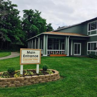 A building entrance with a sign surrounded by a well-maintained lawn and trees.