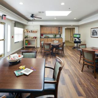 A well-lit dining and kitchenette area with wooden floors and multiple tables and chairs.