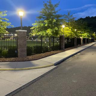 A serene evening scene featuring a well-lit pathway alongside a fence and trees.