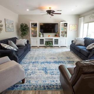 A cozy living room featuring two sofas, an armchair, a large rug, and a TV with decorative shelving units.