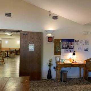 A cozy waiting area featuring a wooden desk with brochures and a lamp, decorated with vases, next to an open doorway leading to a seating area.