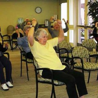 A group of seniors engaging in seated exercises in a community room.
