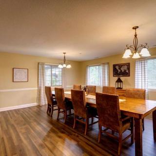A spacious dining room with a large wooden table and chairs, illuminated by chandeliers.