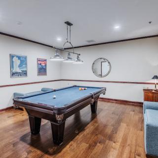 A stylish billiard room featuring a pool table, wooden floors, modern lighting, and decorative wall art.