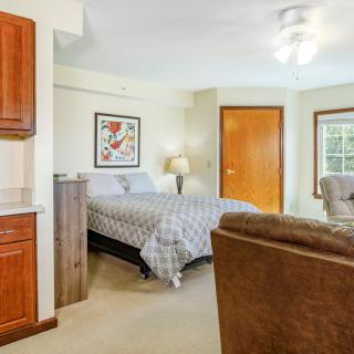 A cozy bedroom with modern furnishings, featuring a comfortable bed, an armchair, a bedside lamp, and vibrant artwork on the wall.