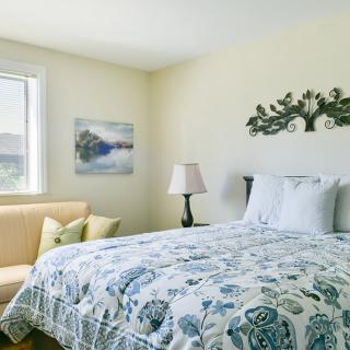 A cozy bedroom featuring a floral-patterned bed, wall art, and a comfortable couch by the window.