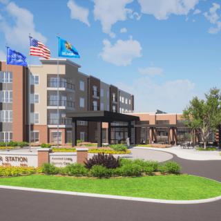 A modern building with flags at the entrance, surrounded by landscaped greenery under a blue sky.