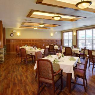 A cozy dining room with several tables and chairs, featuring elegant lighting and wooden floors.