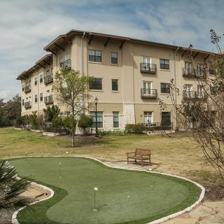 A three-story residential building with a small golf putting green and landscaped garden.