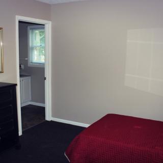 A simple bedroom with a red bedspread, dresser, and an open doorway leading to a bathroom.