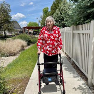 A senior woman enjoying a sunny day while using a walker on a garden pathway.