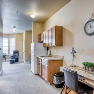 A cozy apartment interior featuring a compact kitchen area with wooden cabinets, a refrigerator, and a small desk setup.