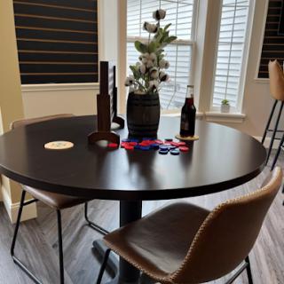 A cozy dining setup featuring a round black table adorned with decorative flowers and game pieces, complemented by stylish chairs.