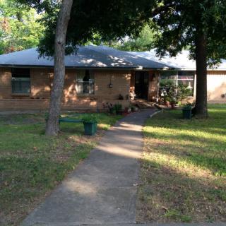 A cozy brick house with a pathway leading through the front yard surrounded by trees.