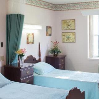 A hospital room with two beds, floral decorations, and vintage furniture.